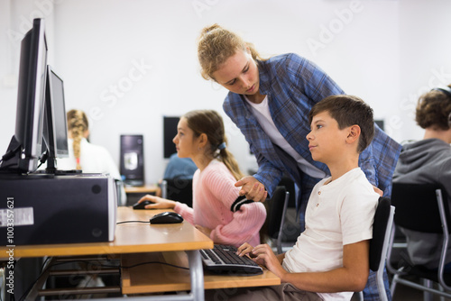 Teenager girl helping younger boy with computer trouble in computer classroom. photo