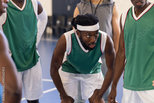 Listening to coach, African American basketball players in green jerseys strategizing during game photo