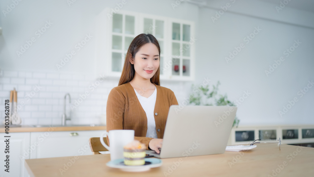 Beautiful young Asian woman working with laptop computer in home kitchen. Work at home Beautiful young Asian woman working with laptop computer in home kitchen. Work at home