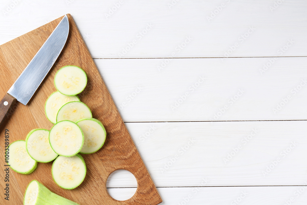 Board with fresh cut zucchini and knife on white wooden table, top view. Space for text Board with fresh cut zucchini and knife on white wooden table, top view. Space for text