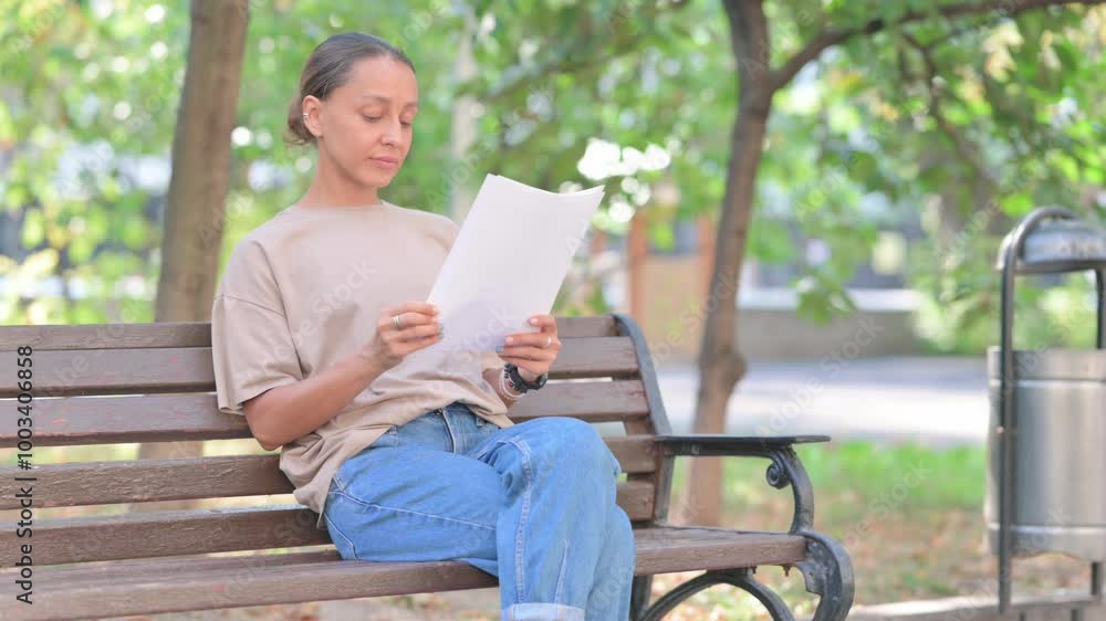 Young Hispanic Woman Reading Documents while Sitting Outdoor on Bench Young Hispanic Woman Reading Documents while Sitting Outdoor on Bench