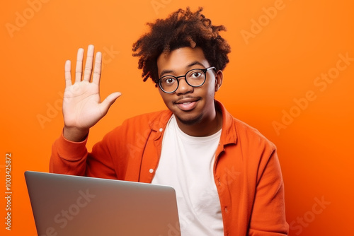 Young Man With Laptop Waving Hello On Orange Background