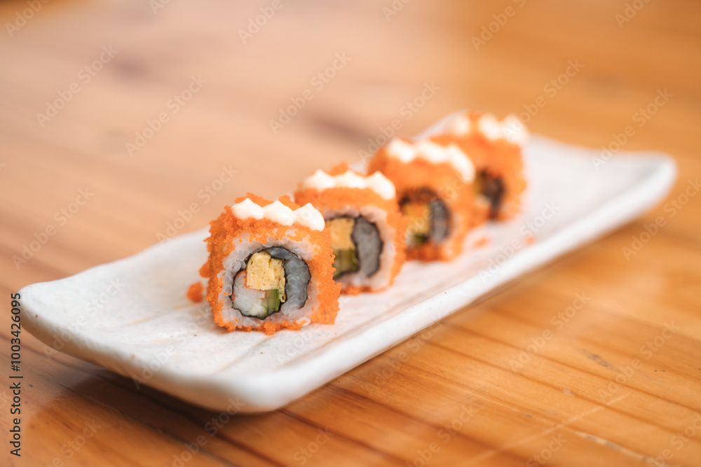 Four pieces of California roll sushi topped with mayonnaise on a rectangular plate. Four pieces of California roll sushi topped with mayonnaise on a rectangular plate.