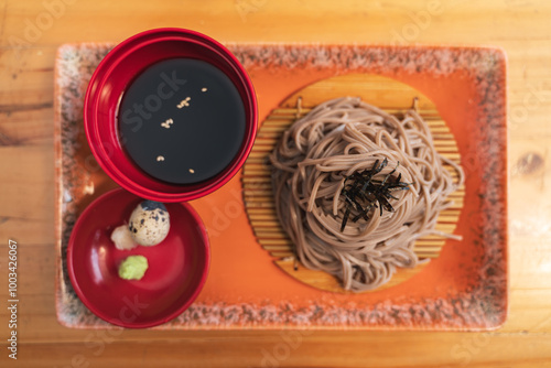 A traditional Japanese dish of chilled soba noodles served with dipping sauce, quail egg, and wasabi on a wooden tray. photo