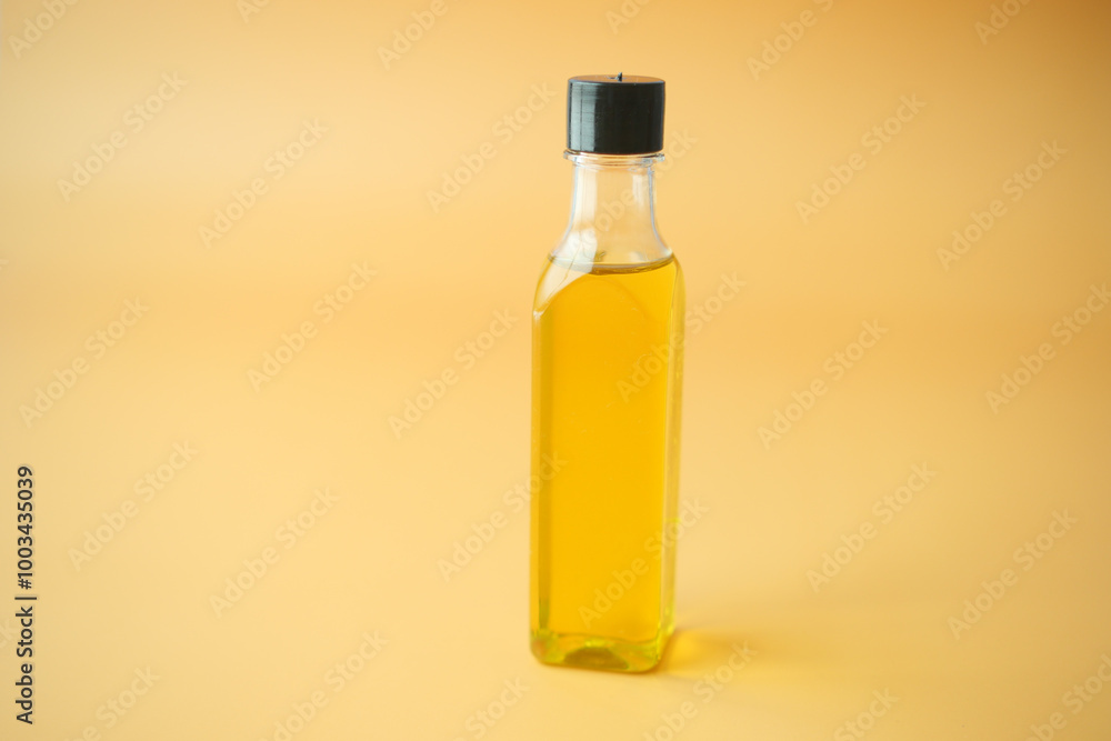 A Clear Glass Bottle filled with Cooking Oil set against a Bright Yellow Background A Clear Glass Bottle filled with Cooking Oil set against a Bright Yellow Background