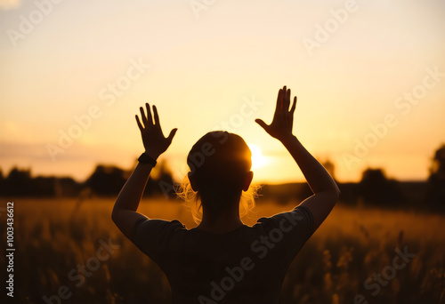 Silhouette of woman raised hands at autumn sunset meadow background