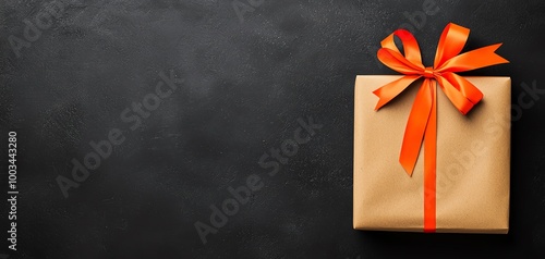 A beautifully wrapped gift box with an orange bow on a dark background, perfect for celebrations and special occasions.