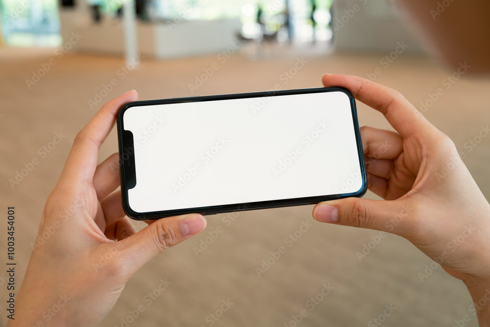 Hand holding black smartphone with blank screen for graphic display montage at shopping mall background. Hand holding black smartphone with blank screen for graphic display montage at shopping mall background.