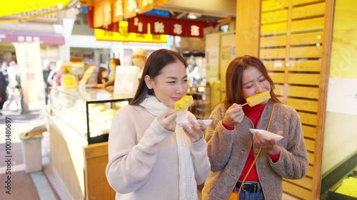 Asian woman friends eating street food sweet egg roll together while travel at fish market in Tokyo city, Japan. Attractive girl enjoy and fun outdoor lifestyle travel street market on autumn vacation