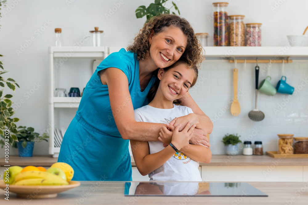 Cute mother and daugther hugging while looking at camera in the kitchen at home Cute mother and daugther hugging while looking at camera in the kitchen at home
