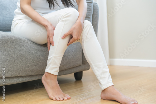 Muscle pain or leg pain, suffer asian young woman, girl hand massaging brawn leg calf muscle cramps or spasm, trauma from inflammation of tendon at calves while sitting on sofa. Health care concept.