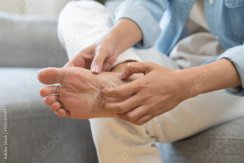 Foot pain, ache asian young woman hand scratch feet, itch foot, problem itchy skin on carpet at home, dermatitis from fungus, fungal bacterial infection, allergic reaction, eczema. Foot care concept. photo