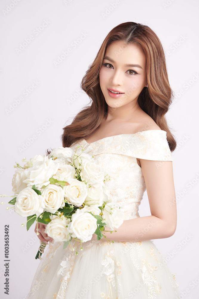Naklejka premium Beautiful young asian woman in wedding dress holding bouquet on white background,