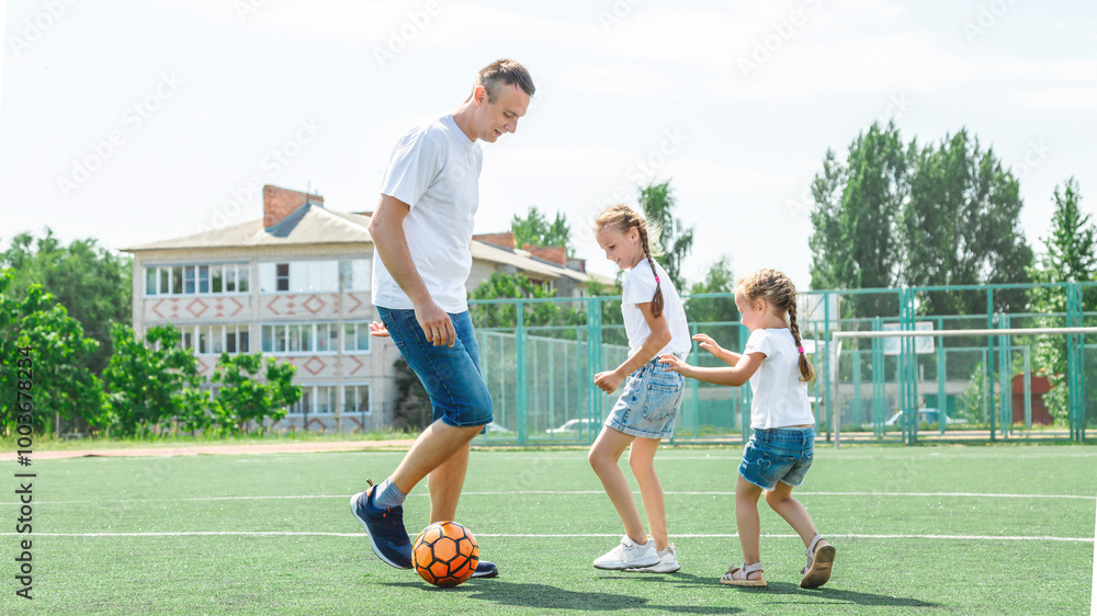 Obraz premium Father and daughters playing in the sport stadium at the daytime. Concept of friendly family. Picture made on the sport field