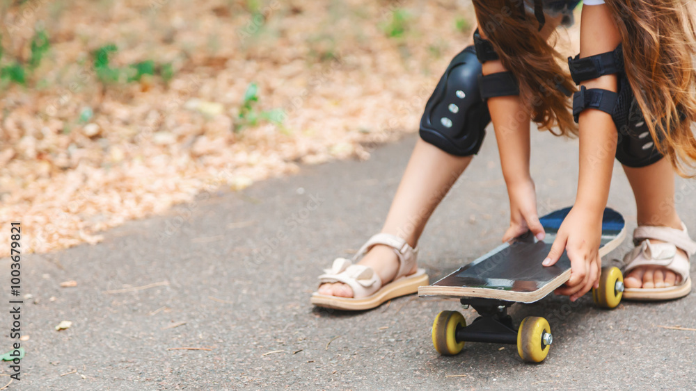 Obraz premium Active child girl in casual wear practicing skateboard tricks on street embracing her penny board in the park looking away with charming smile