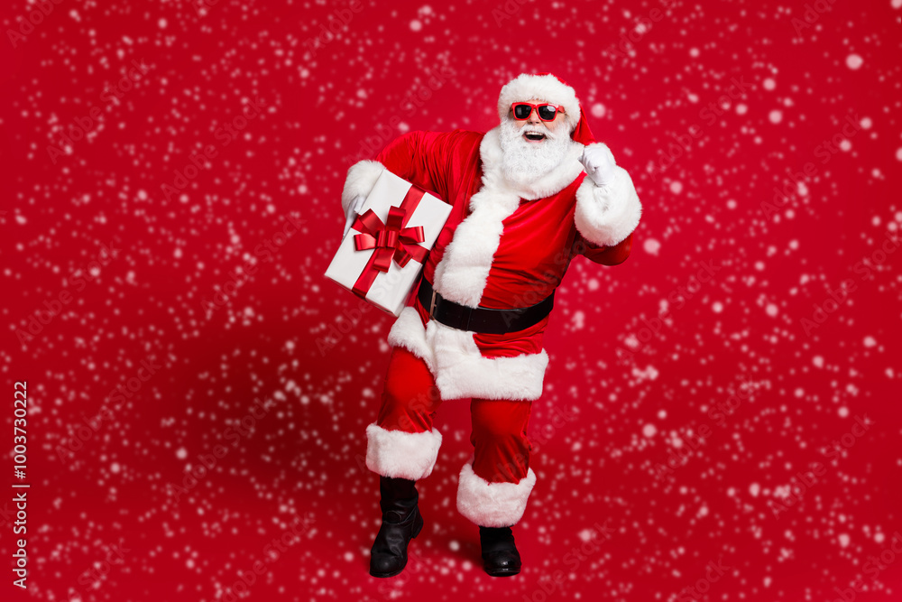 Full length photo of retired old man white beard walk kindergarten hold box bow-knot present children wear x-mas santa costume glove coat belt sunglass cap boot isolated red color background Full length photo of retired old man white beard walk kindergarten hold box bow-knot present children wear x-mas santa costume glove coat belt sunglass cap boot isolated red color background