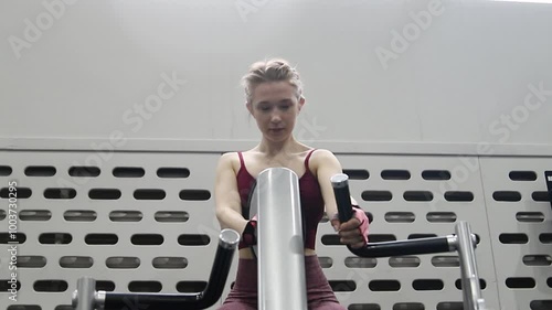 Young attractive woman trains her arms on a machine in a gym.