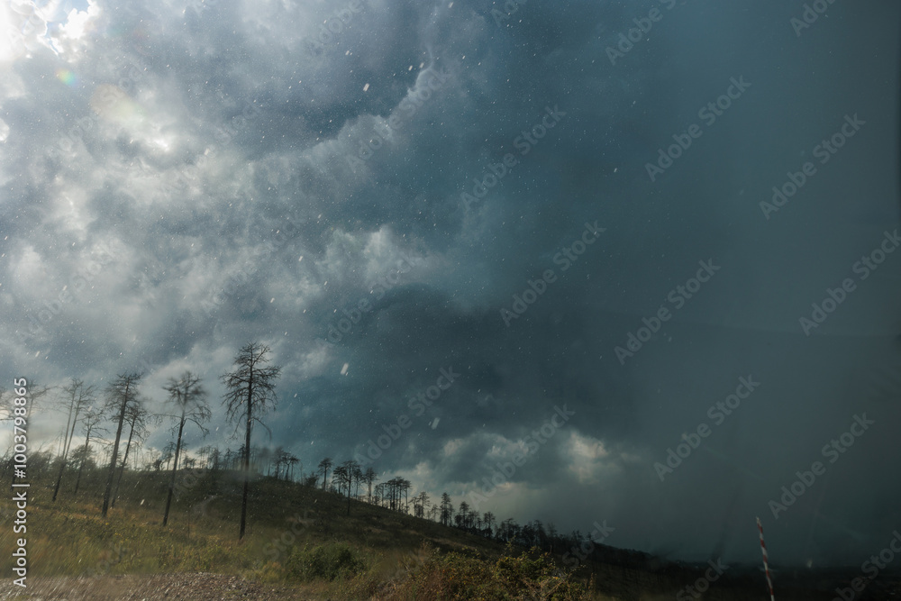 vista panoramica su un ambiente collinare durante l'arrivo di un forte temporale estivo che oscura il cielo, tra Italia e Slovenia, mentre la pioggia cade