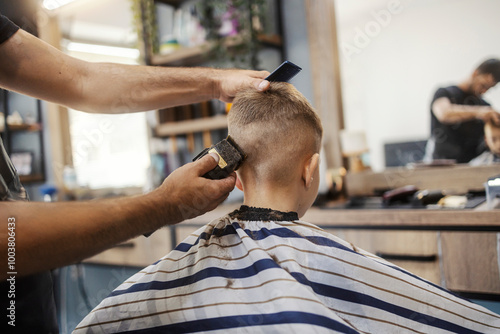 Haircut day. Hairdresser is giving new haircut to a little boy at barber shop.