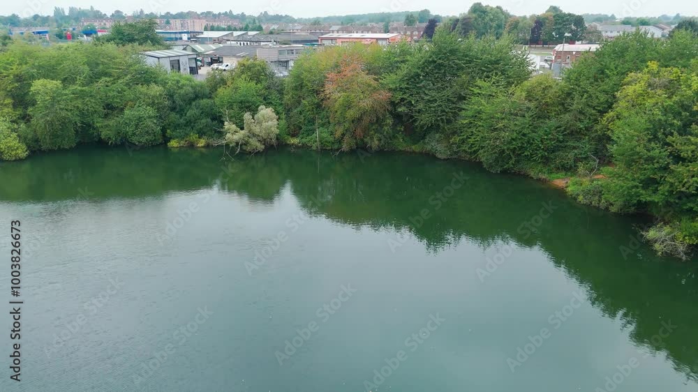 Aerial shot capturing an urban landscape and a calm body of water bordered by lush greenery. The overcast sky and industrial buildings add a contrasting touch to the tranquil scene Aerial shot capturing an urban landscape and a calm body of water bordered by lush greenery. The overcast sky and industrial buildings add a contrasting touch to the tranquil scene