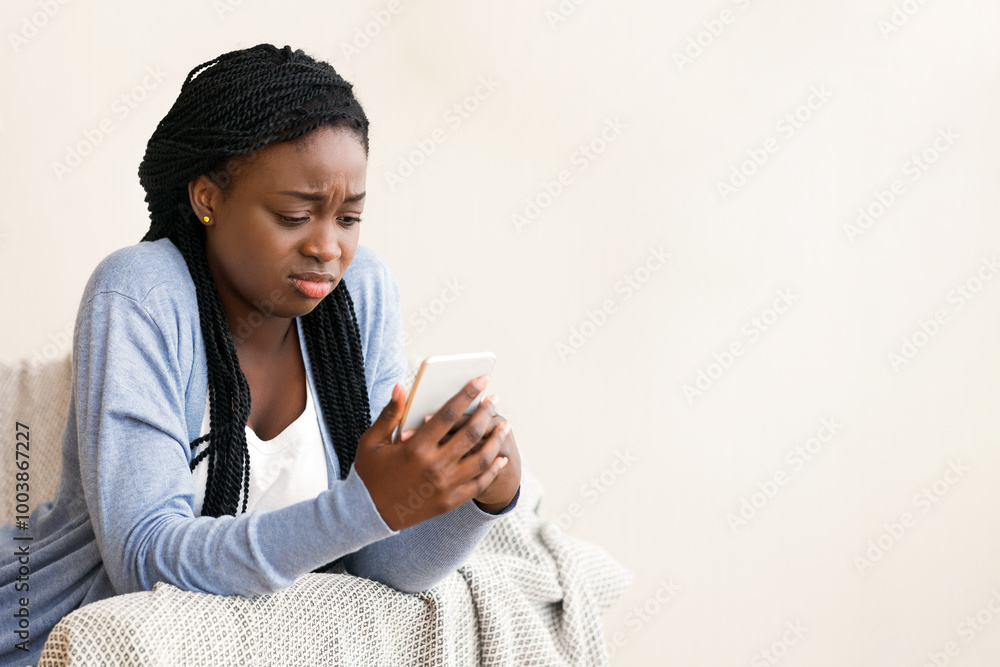 Bad message. Young black woman looking at smartphone screen with sad face expression, free space Bad message. Young black woman looking at smartphone screen with sad face expression, free space