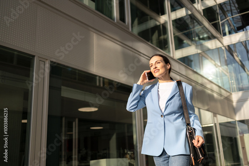 Businesswoman strolls outside her office building, engaged in a phone conversation