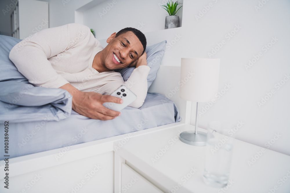 Photo of nice young man lying bed hold device wear pajama enjoy wake up modern cozy interior bedroom indoors Photo of nice young man lying bed hold device wear pajama enjoy wake up modern cozy interior bedroom indoors