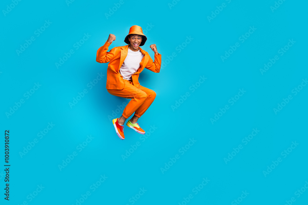 Photo of excited trendy guy jumping up winning raise fists wear stylish clothes isolated blue color background Photo of excited trendy guy jumping up winning raise fists wear stylish clothes isolated blue color background