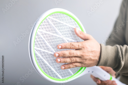 A Man is holding the swatter and touching its circuit, Whether it poses a physical danger to the human body. Concept explores whether a person can touch the circuit of an electric mosquito swatter photo