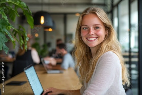 Young blonde woman smiling and looking at camera while working on her laptop.