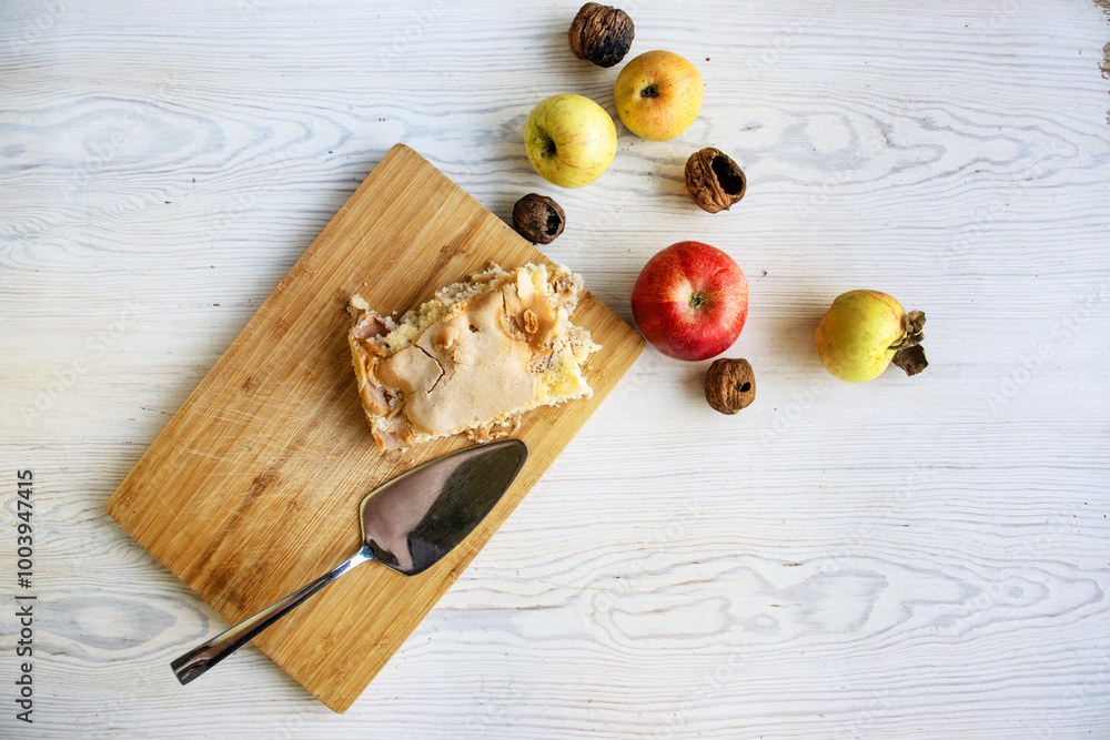 Piece of traditional thanksgiving apple cinnamon pie on the wooden cutting board on the white table, surrounded by fresh apples and walnuts. Autumn dessert. Closeup. Copy space. Top view Piece of traditional thanksgiving apple cinnamon pie on the wooden cutting board on the white table, surrounded by fresh apples and walnuts. Autumn dessert. Closeup. Copy space. Top view