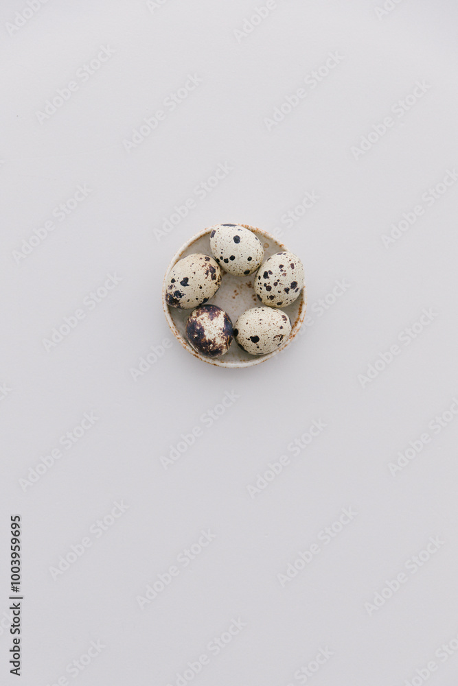Five quail eggs in a small bowl on a light grey table top.