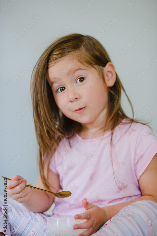 A girl child eats ice cream sitting on the bed. Rejoices, grimaces, enjoys. Holiday, weekend, home A girl child eats ice cream sitting on the bed. Rejoices, grimaces, enjoys. Holiday, weekend, home