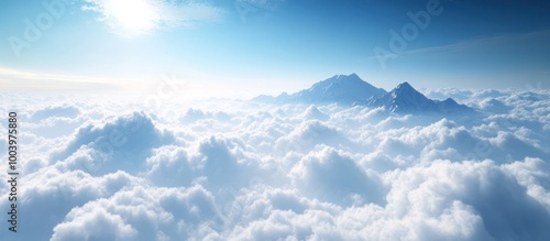 A breathtaking aerial view of a mountain peak rising above a sea of fluffy white clouds with a blue sky and sun above.