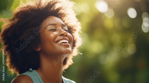 A young woman radiates bliss as she beams a joyful smile, her curly hair illuminated by the soft, golden sunlight against a blurred, natural green backdrop.