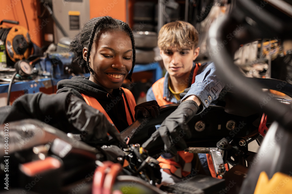Two young mechanics, one male and one female, working together on engine repairs in a garage, wearing safety vests. Diverse Young Mechanics Working on Engine in Garage Two young mechanics, one male and one female, working together on engine repairs in a garage, wearing safety vests. Diverse Young Mechanics Working on Engine in Garage