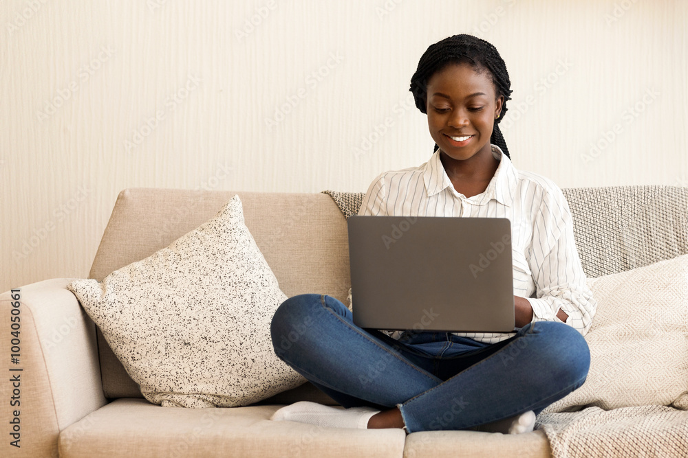Smiling african american freelancer working on laptop computer on sofa at home, free space