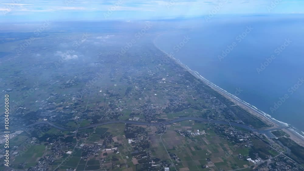 Coastline and farmland stretching across a wide landscape beneath a cloudy sky, aerial view