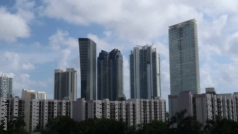 A timelapse captures the skyline of Sunny Isles, Miami, showcasing tall buildings under a sunny sky with drifting clouds, highlighting the dynamic urban landscape. A timelapse captures the skyline of Sunny Isles, Miami, showcasing tall buildings under a sunny sky with drifting clouds, highlighting the dynamic urban landscape.