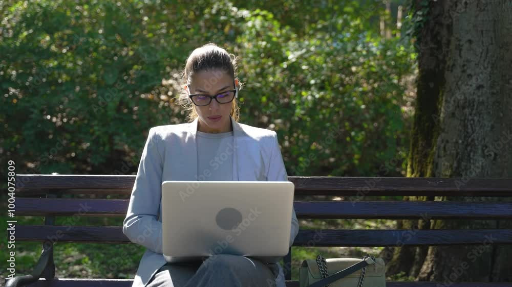 Young business woman CEO sitting in park on bench working on laptop computer. Businessperson freelancer taking a break from office work finishing job during lunch break. Design professional occupation Young business woman CEO sitting in park on bench working on laptop computer. Businessperson freelancer taking a break from office work finishing job during lunch break. Design professional occupation