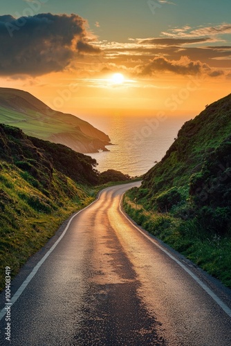 A beautiful road leading to the horizon, with green hills and cliffs on both sides of it. The sun is setting in front of you. In the distance behind you lies an ocean