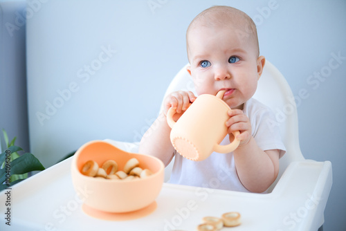 Fotografía baby sitting in high chair, drinking clean water from baby sippy cup