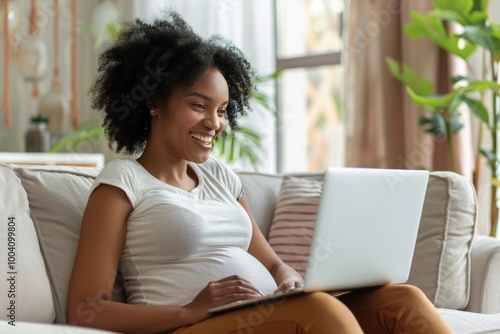 A pregnant woman sits comfortably on a couch, typing away on her laptop