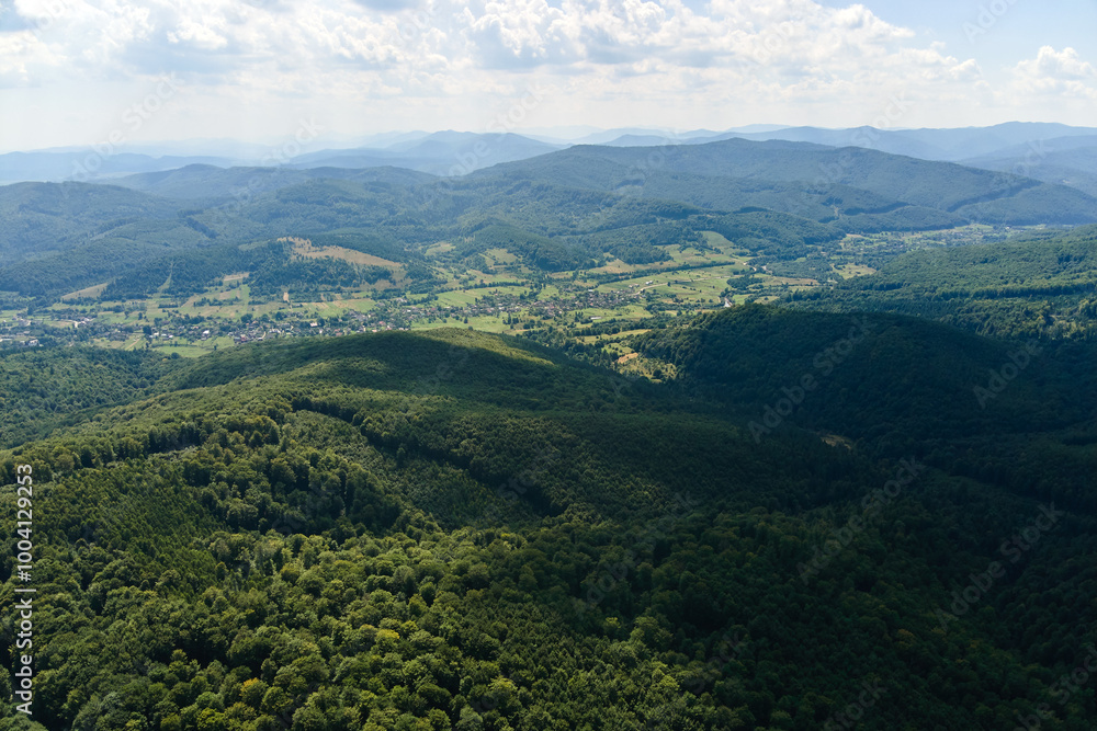 Fototapeta premium Aerial view of mountain hills covered with dense green lush woods on bright summer day