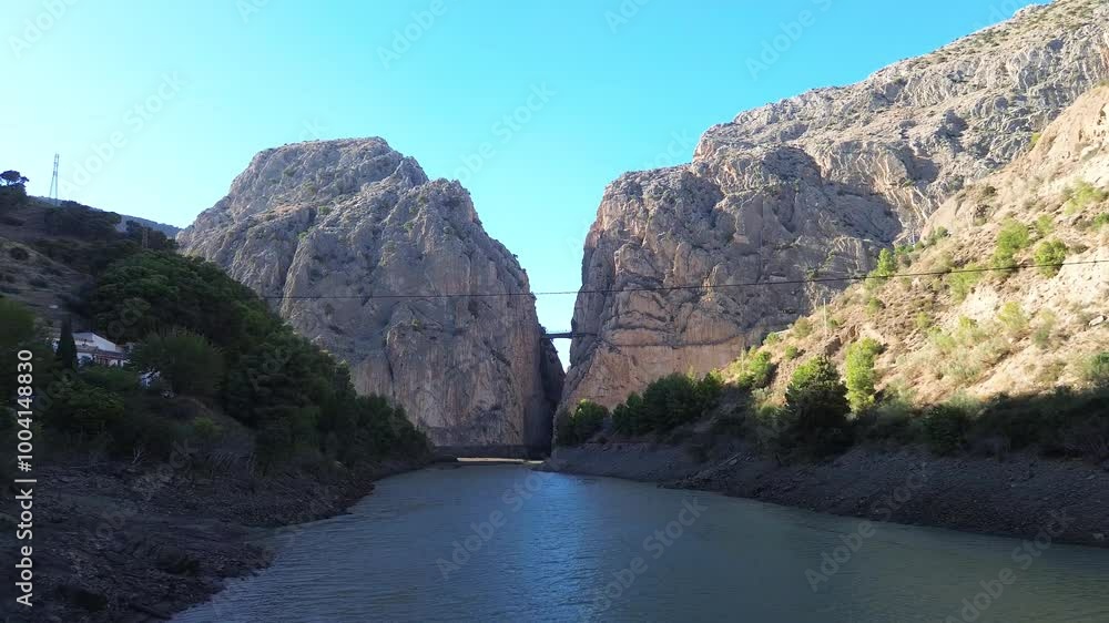 Drone flight over the river to the gorge Garganta del Chorro and Caminito del Rey, Spain. A bridge in a narrow gorge between huge high mountains, green forest on the river banks. Drone flight over the river to the gorge Garganta del Chorro and Caminito del Rey, Spain. A bridge in a narrow gorge between huge high mountains, green forest on the river banks.