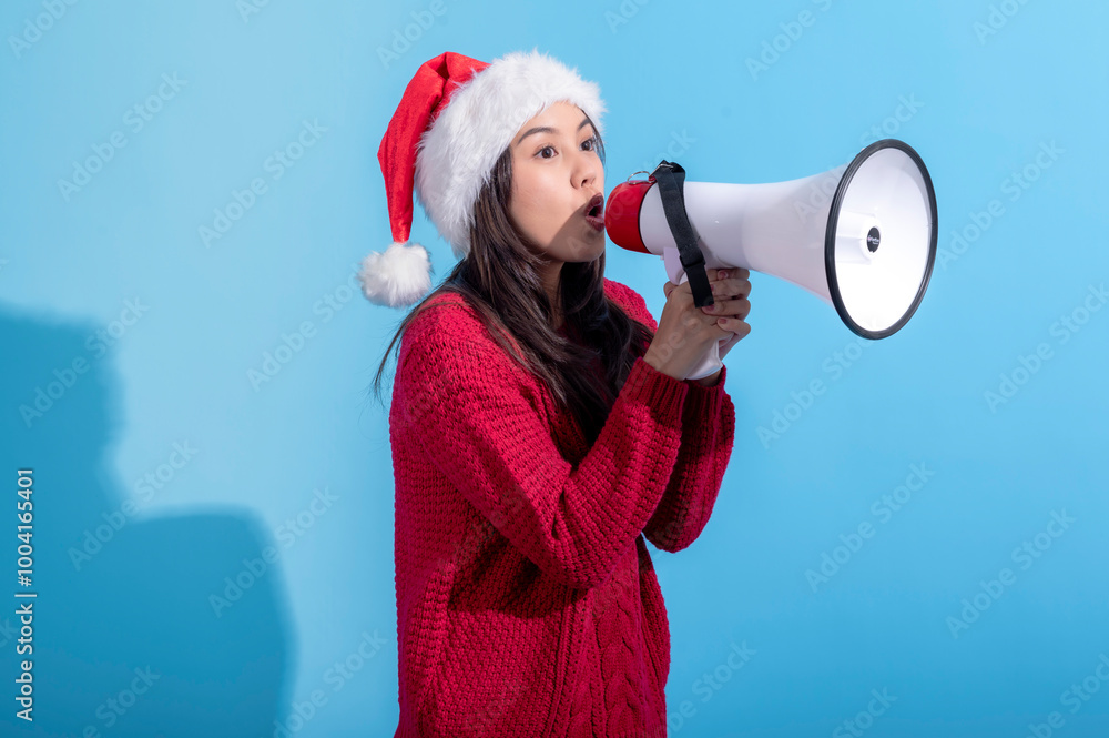 An Asian woman, wearing a Santa hat and a red knitted sweater, is speaking excitedly through a large white megaphone with a red front. She stands against a light blue background. An Asian woman, wearing a Santa hat and a red knitted sweater, is speaking excitedly through a large white megaphone with a red front. She stands against a light blue background.