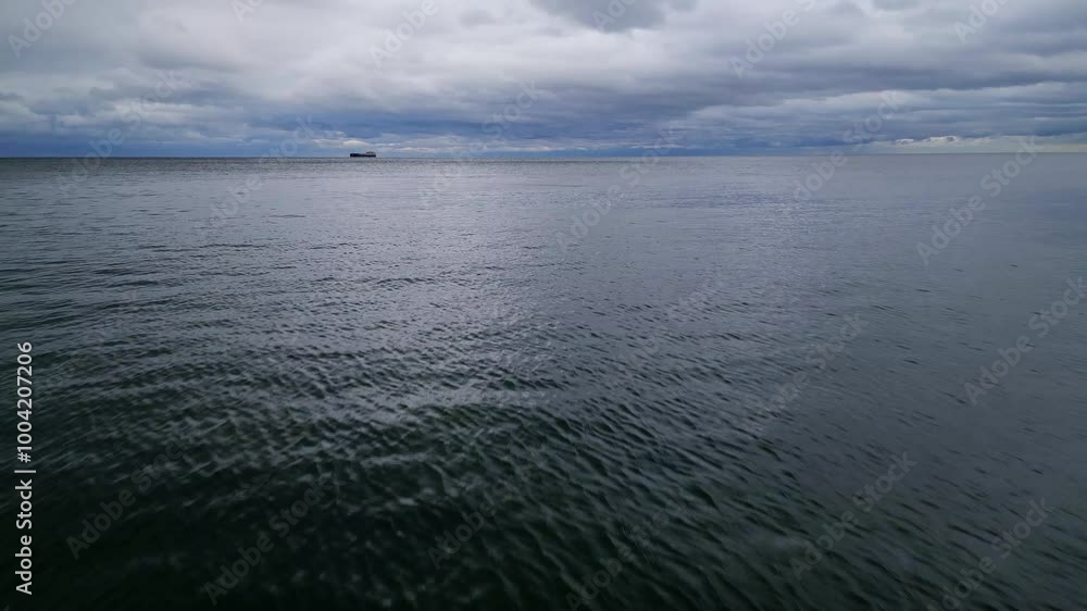 Aerial drone view of a calm sea with distant clouds and a lone ship on the horizon. The tranquil water and moody sky create a peaceful, atmospheric scene Aerial drone view of a calm sea with distant clouds and a lone ship on the horizon. The tranquil water and moody sky create a peaceful, atmospheric scene