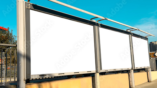Three blank billboard frames side by side on a sidewalk, ready for advertisements, under a bright blue sky.