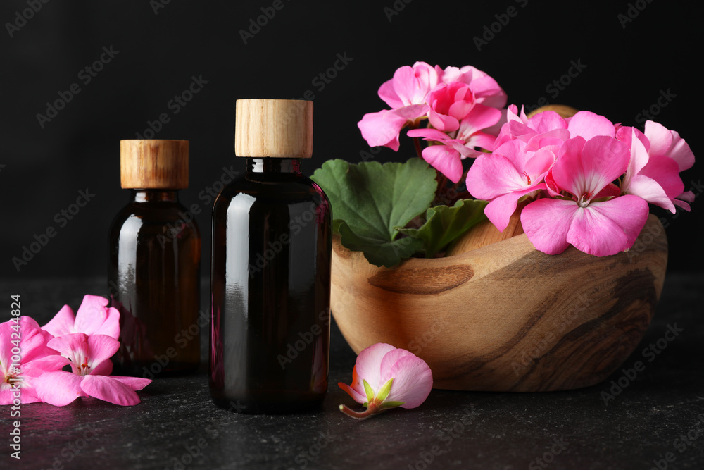 Bottles of geranium essential oil and beautiful flowers on black table, closeup Bottles of geranium essential oil and beautiful flowers on black table, closeup