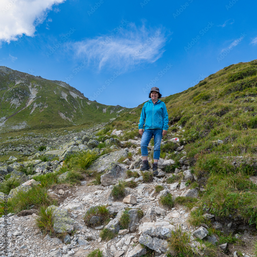 Woman on the way through beautiful mountain meadows with alpine autumnal flowers. the hiker on the footpath climbs the stony path up to the summit. beautiful alpine landscape with view over Austria Woman on the way through beautiful mountain meadows with alpine autumnal flowers. the hiker on the footpath climbs the stony path up to the summit. beautiful alpine landscape with view over Austria